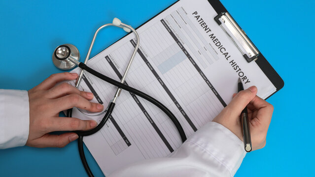 Focused doctor hand holding stethoscope and writing medical report on paper clipboard with pen during patient consultation
