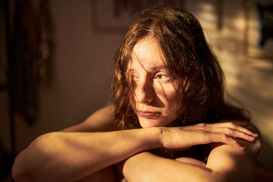 Young adult Caucasian woman sitting with arms crossed looking away thoughtfully, representing mental health and introspection, suitable for wellness and therapy campaigns, close up shot