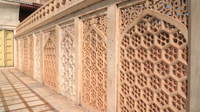 Horizontal pan left shot of intricately carved sandstone jali lattice screens along a balcony at Agra Fort in Uttar Pradesh, India.