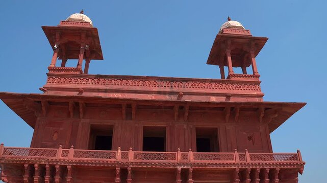 Smooth pan low angle shot of the ornate red sandstone facade and domed chhatri pavilions of Jahangiri Mahal at Agra Fort in Uttar Pradesh, India.