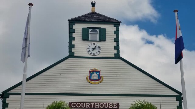 Bell tower of Philipsburg Courthouse on Front Street in Sint Maarten, showcases iconic Caribbean colonial architecture, white wood facade, green accents and clock tower topped by a golden pineapple