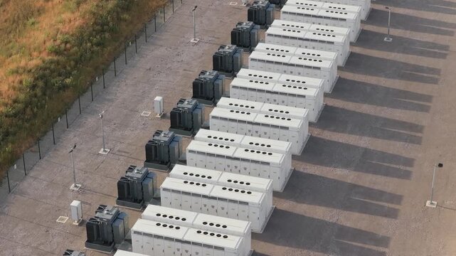 Aerial view of rows of industrial lithium ion battery containers in a storage facility during a bright sunny afternoon with long shadows cast across the concrete surface of the grid area