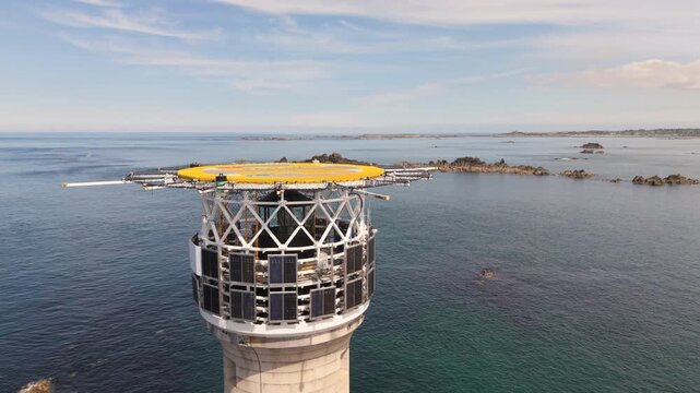 Hanois Lighthouse,Guernsey,Channel Islands.Slow rising flight over helipad on top of lighthouse with clear calm sea and granite rocks and view of coastline in bright sun with misty horizon