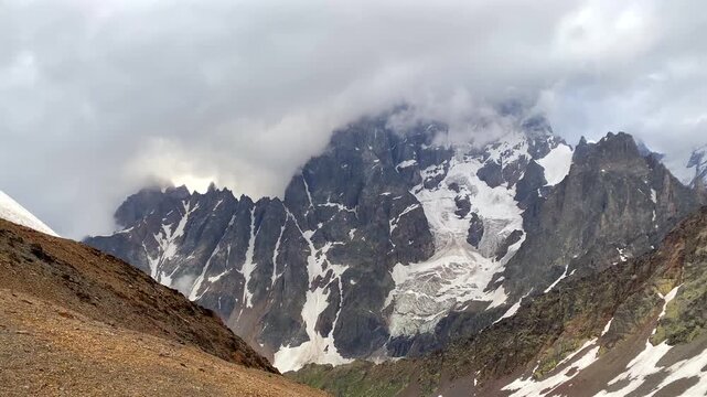 Clouds covering Mount Ushba in wide view above snow-covered slopes in Svaneti, Georgia, mountain weather scene for trekking forecasts, expedition planning, alpine tourism, and geography media.