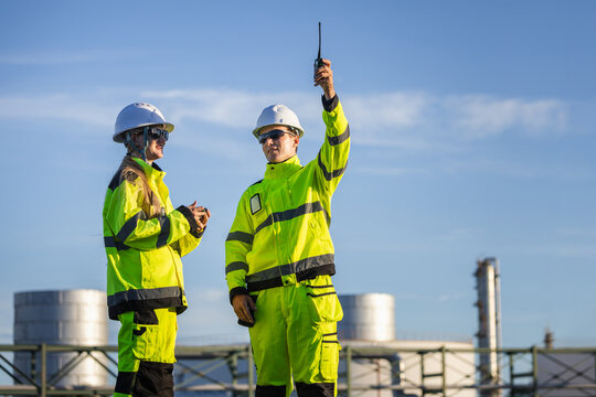 Oil refinery engineers with walkie talkie communication outdoors at plant, Petroleum plant workers using radio communication at facility, Energy industry professionals discussing work at site