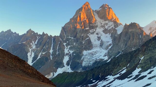 Mount Ushba glowing in wide shot, sunrise light covering snow and rock in Svaneti, Georgia for travel promotion, alpine tourism branding, mountain weather media use, and destination marketing.