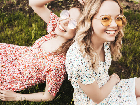 Two young beautiful smiling hipster in trendy summer sundress.Sexy carefree women lying on the green grass in sunglasses.Positive models having fun.Top view