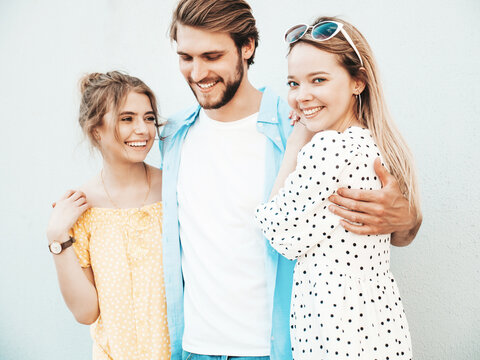 Group of young three stylish friends posing in the street. Fashion man and two cute girls dressed in casual summer clothes. Smiling models having fun near wall.Cheerful women and guy outdoors