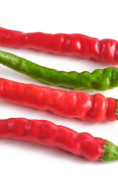 Close up shot long red and green hot chili peppers arranged diagonally on bright white background.
