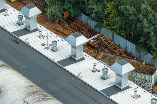 Aerial view of a flat industrial roof featuring metallic ventilation ducts and chimneys.