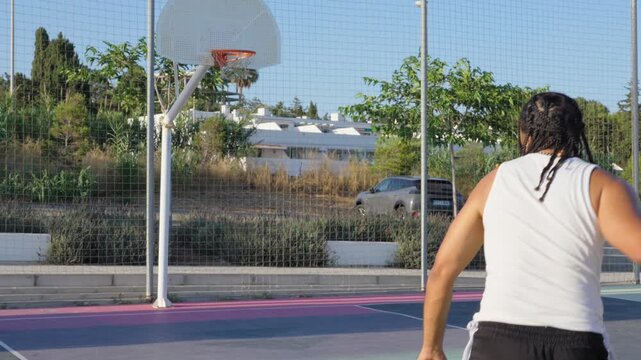 Athletic man playing basketball on outdoor court