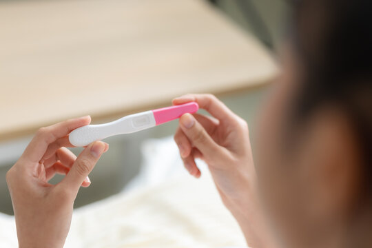 Woman holding pregnancy test at home while checking the result, representing pregnancy, fertility, family planning, reproductive health and an important personal healthcare moment.