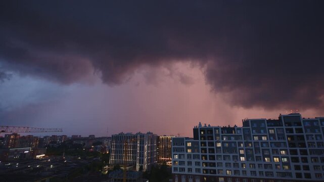 Lightning flashes over the buildings in a city. Rain and thunder storm over the city.
