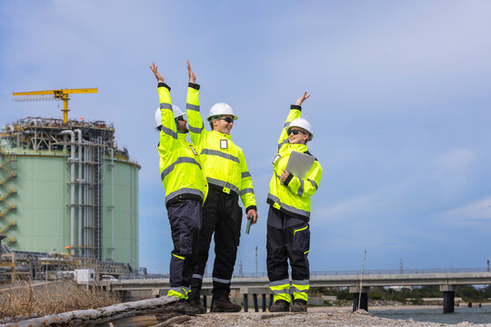 LNG plant engineers team celebrating success with hands raised outdoors, Liquefied natural gas plant workers happy and cheering at industrial facility, Industry professionals celebrating achievement