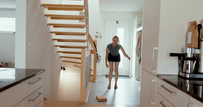 Woman accidentally drops a cardboard package and bends down to pick it up, representing parcel handling, delivery accidents, damaged goods, and everyday mistakes.