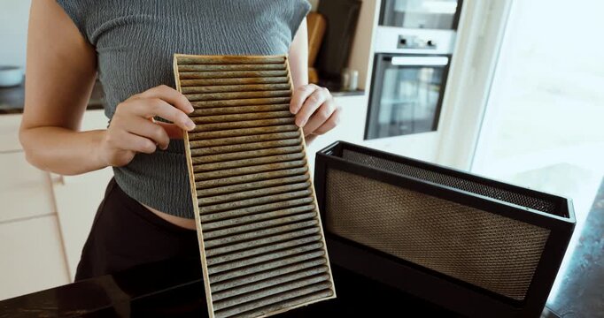 Woman holding a heavily dirty and greasy kitchen extractor filter, representing grease buildup, neglected maintenance, kitchen hygiene, and filter cleaning.