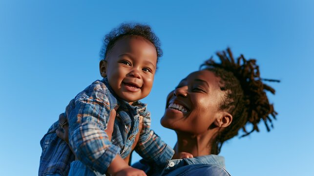 A joyful mother lovingly holds her smiling child against a clear blue sky, capturing a moment of happiness.