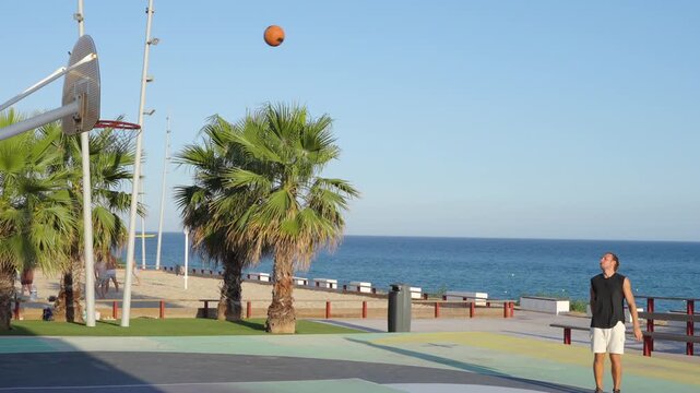 Young man scoring basket on seaside court