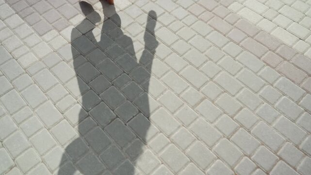 Close up of person shadow walking on light colored brick pavement showing subtle movement and changes in position. scene features consistent daylight lighting with no visible background