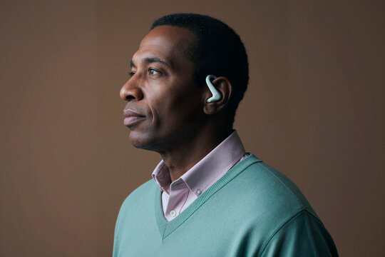 Middle aged Black man wearing wireless earbud and looking away in profile, suggesting hands free communication and audio technology use. Ideal for tech marketing and connectivity themes