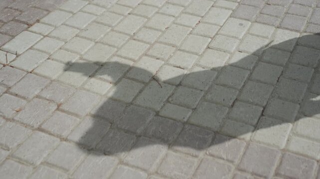 Close up of person feet in high heels walking on gray cobblestone pavement showing shadow cast by their movement. scene focuses solely on foot motion and ground texture with no other visible