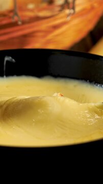 bread dipped in melted cheese fondue lifted with stretchy cheese strings closeup, vertical video