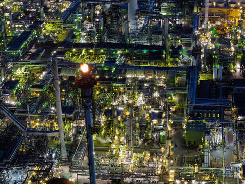 Aerial view of an industrial oil refinery at night with illuminated processing units, pipelines, and a bright flare stack burning in the United Kingdom.