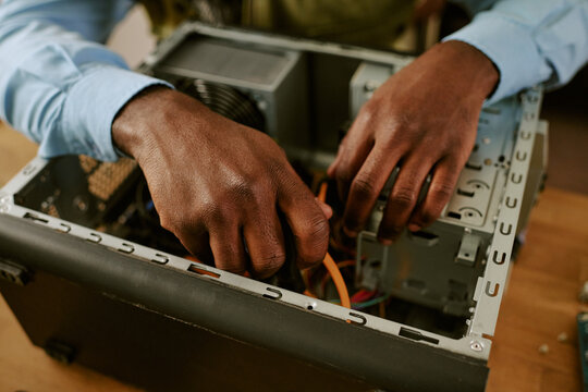 Hands of Black male technician repairing hardware inside retro computer system unit. Close up shot highlighting technical support, hardware maintenance and computer repair services