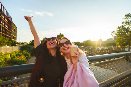 Two friends laughing, having fun outdoors with takeaway coffee at golden hour