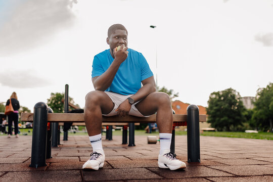 Young black man eating apple in outdoor gym