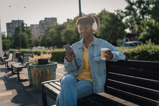 Young woman enjoying music and coffee in city park