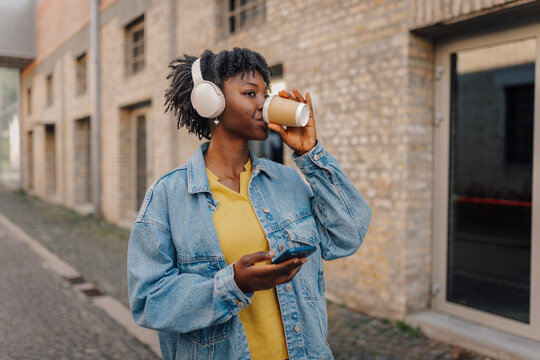 Black woman drinking coffee wearing headphones urban lifestyle