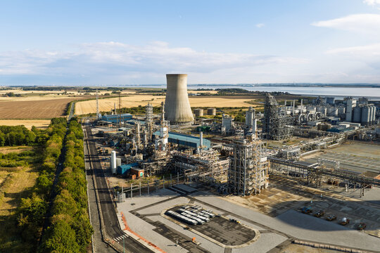 Aerial view of an industrial chemical plant featuring a prominent cooling tower, complex piping networks, and storage tanks, surrounded by agricultural fields in the United Kingdom.