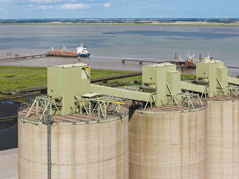 Aerial view of industrial storage silos near a coastal shipping terminal with a tanker vessel in the water in the United Kingdom.