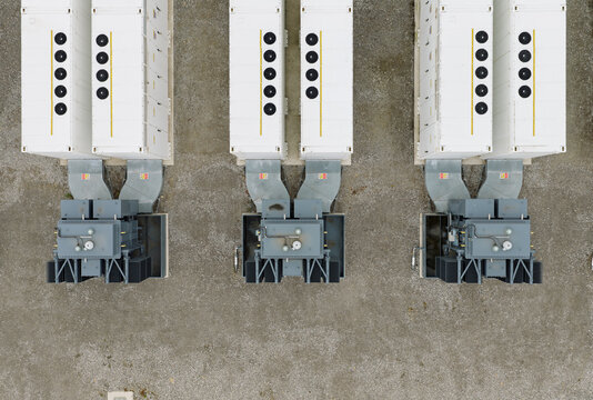 Aerial view of industrial battery energy storage system units with white containers and electrical transformers on a gravel site in the United Kingdom.