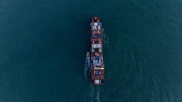 Aerial view of a large container ship loaded with colorful cargo containers navigating through deep blue waters with a small pilot boat trailing behind Lagos, Lagos, Nigeria.