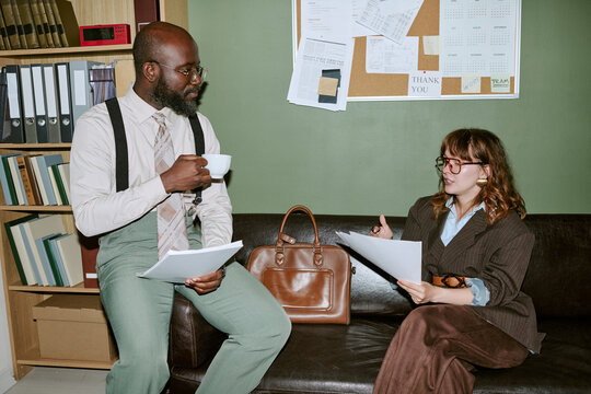 Diverse young adult colleagues discussing documents in retro office setting. Image represents vintage corporate communication and is suitable for business history articles
