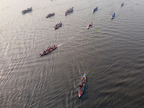 Aerial view of a traditional boat race with many long wooden boats filled with people moving along the river in Gopalganj, Dhaka Division, Bangladesh.