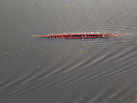 Aerial view of a traditional boat race with rowers in a long wooden boat moving across the dark water in Gopalganj, Dhaka Division, Bangladesh.