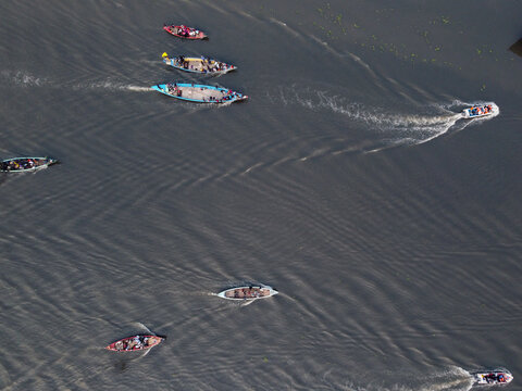 Aerial view of a traditional boat race with long wooden boats moving across the river, creating wakes in the water in Gopalganj, Dhaka Division, Bangladesh.