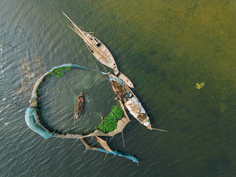 Aerial view of fishermen working in small wooden boats within a circular fishing net structure on the river in Narayanganj, Dhaka, Bangladesh.
