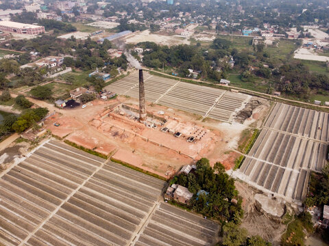 Aerial view of a brick kiln with a tall chimney and rows of drying bricks in a riverside setting in Dhaka, Bangladesh.