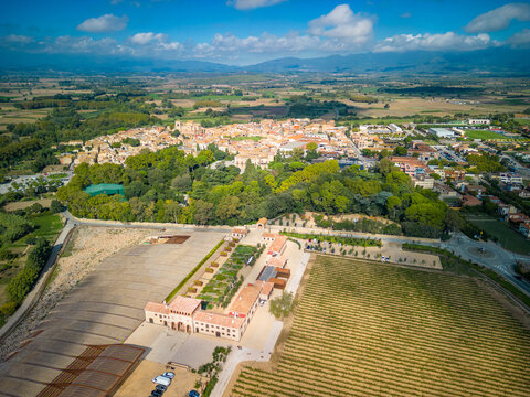 Aerial view of the historic town of Peralada surrounded by lush vineyards, green trees, and agricultural fields under a bright blue sky in Peralada, Catalonia, Spain.