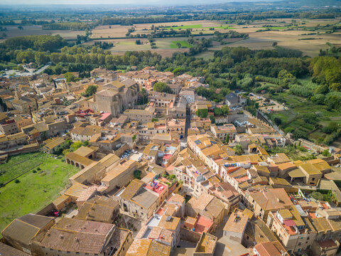 Aerial view of the historic town of Peralada with traditional stone buildings, terracotta rooftops, and narrow streets surrounded by lush greenery and fields in Peralada, Catalonia, Spain.
