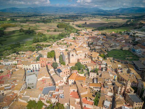 Aerial view of the historic town of Peralada with terracotta rooftops, narrow streets, and a central church tower, surrounded by fields and distant mountains in Peralada, Catalonia, Spain.