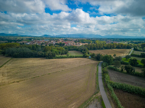 Aerial view of the historic town of Peralada surrounded by agricultural fields, lush trees, and a winding road under a blue sky with white clouds in Peralada, Catalonia, Spain.