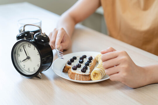 Woman waiting to eat her healthy meal during intermittent fasting concept with alarm clock on wooden table background