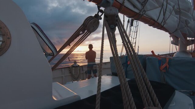Sailing the Atlantic. Male sailor stands on the deck of the big sailing boat moving in the Atlantic Ocean under the sails and enjoys the last light of the day