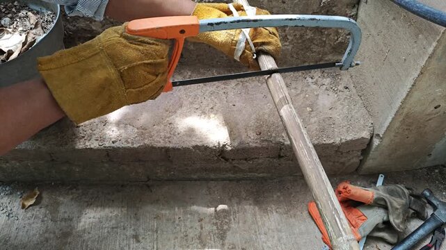 Gloved Hand Cutting Thin Bamboo Stalk with Hacksaw Tool