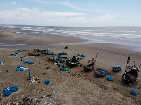 Aerial view of traditional wooden fishing boats with blue nets scattered on the sandy beach along the coastline in Cox's Bazar, Chittagong Division, Bangladesh.